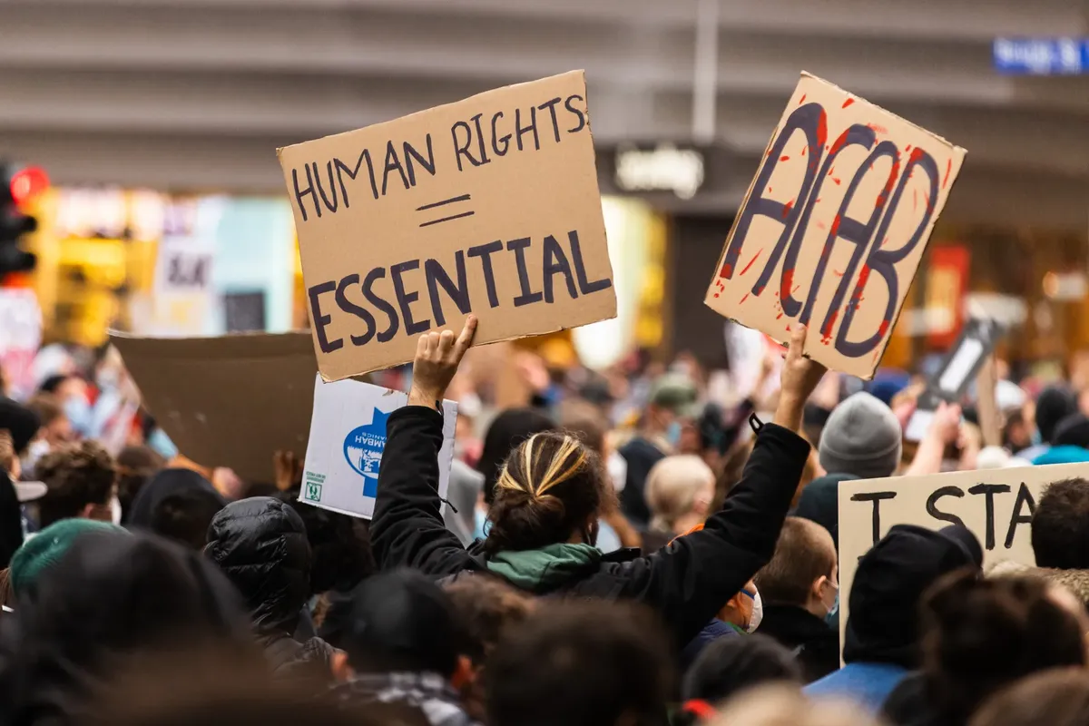 A crowd gathers in Melbourne for a protest advocating human rights, holding signs with powerful messages.